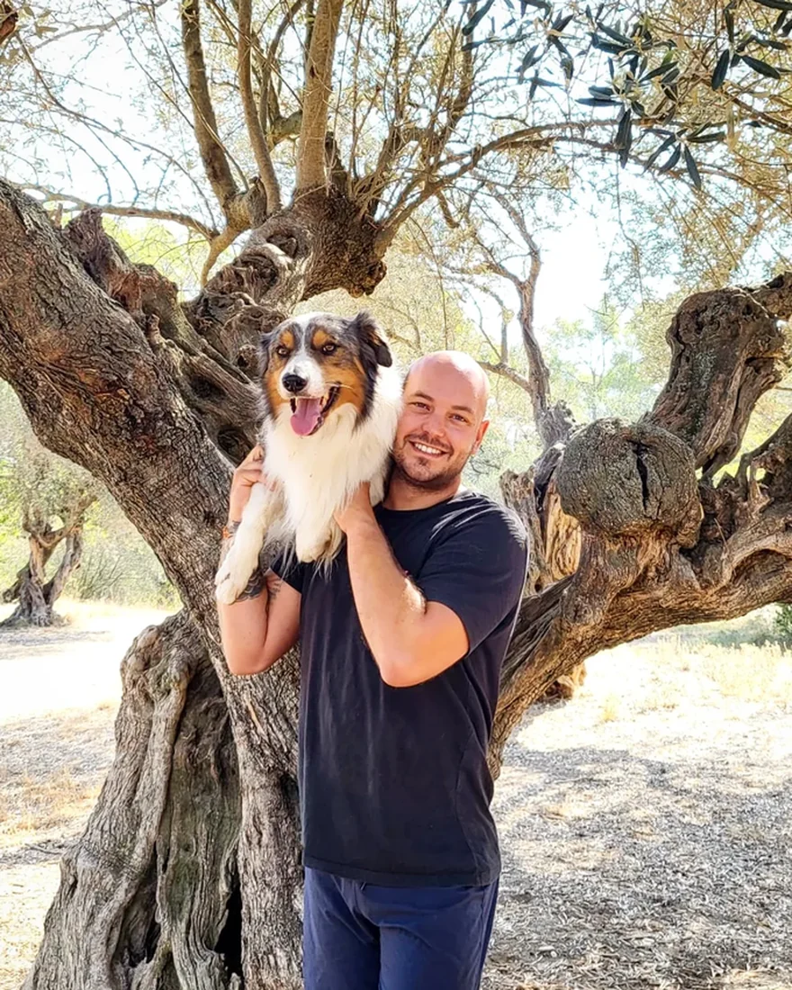 Llorenç Ventura con un perro en brazos, bajo un olivo